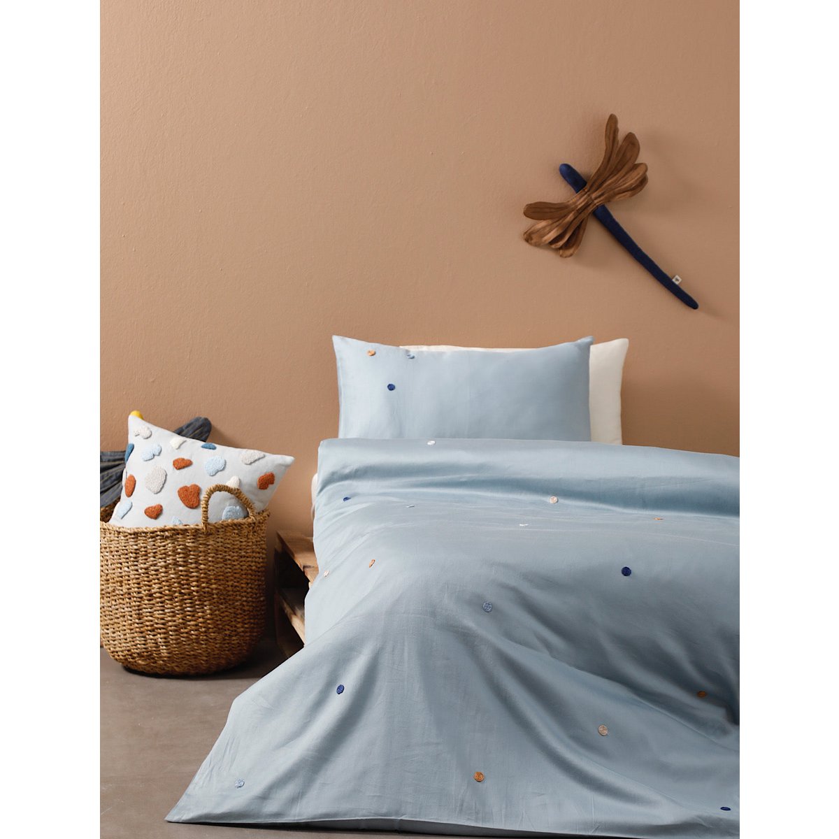 Bed with light blue bedding and pillows against a beige wall.