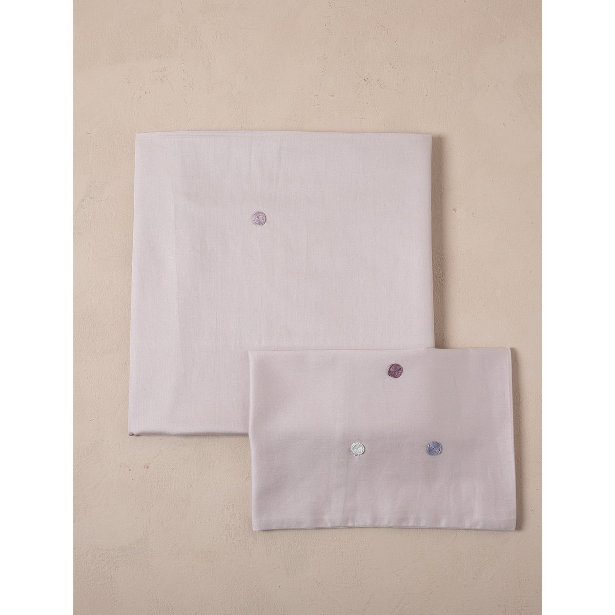 Two light purple fabric items with embroidered stones on a beige background