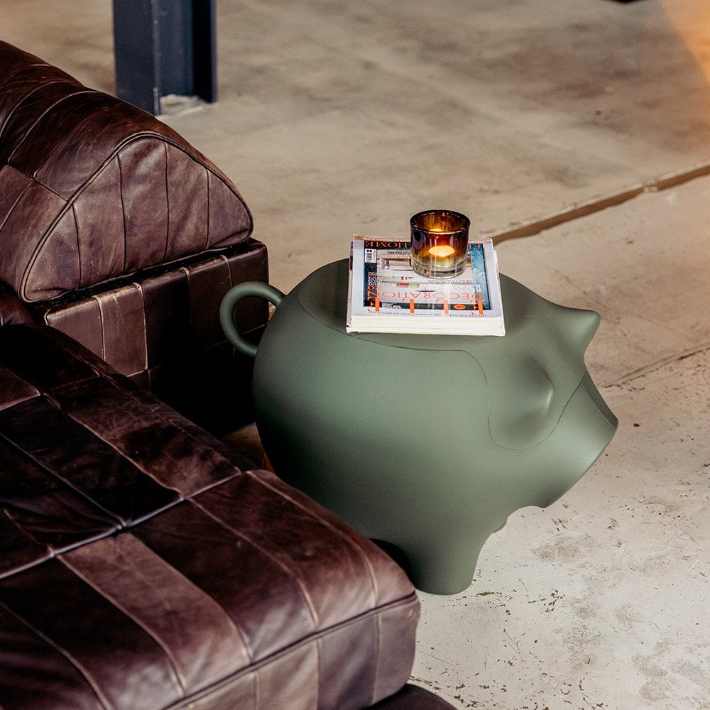 Green animal-shaped side table next to a brown leather sofa with a candle and magazine on top.