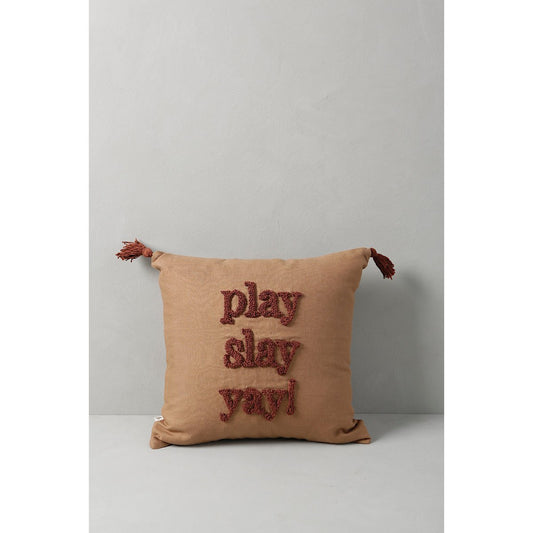 Beige pillow with red text and tassels on a light gray background
