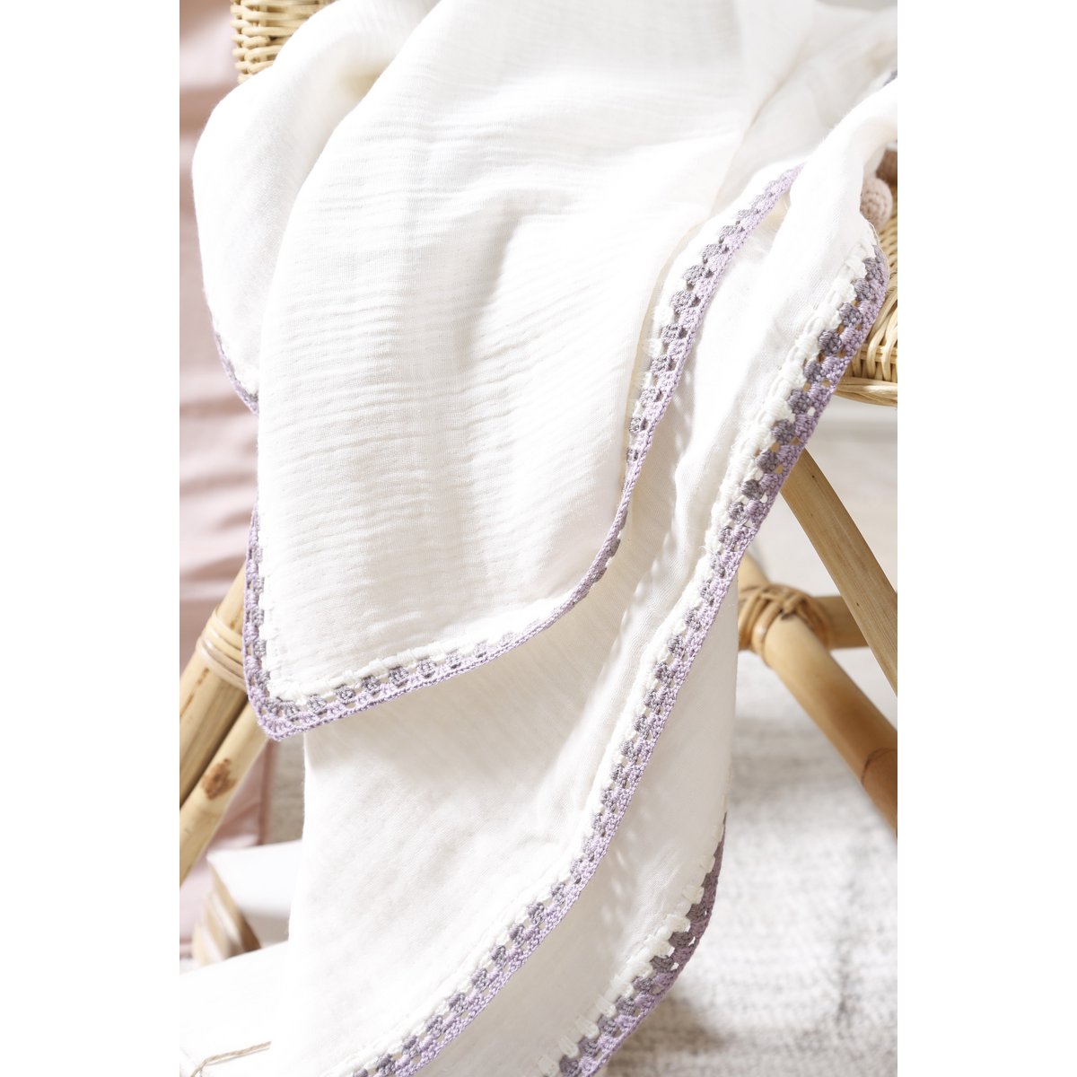 White fabric with purple trim draped over a wicker chair.