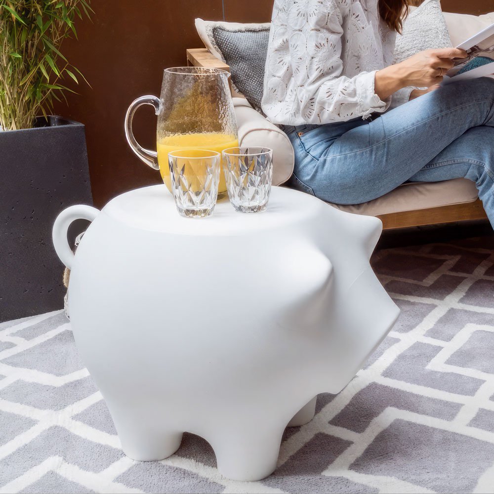 White pig-shaped side table with a pitcher of orange juice and glasses on a patterned rug.