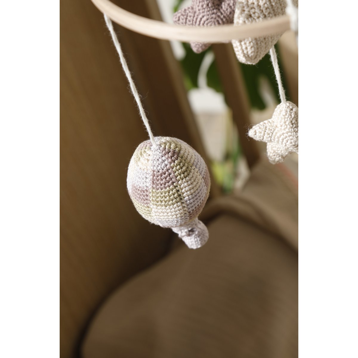Decorative mobile with crocheted balls and stars hanging from a wooden rod.