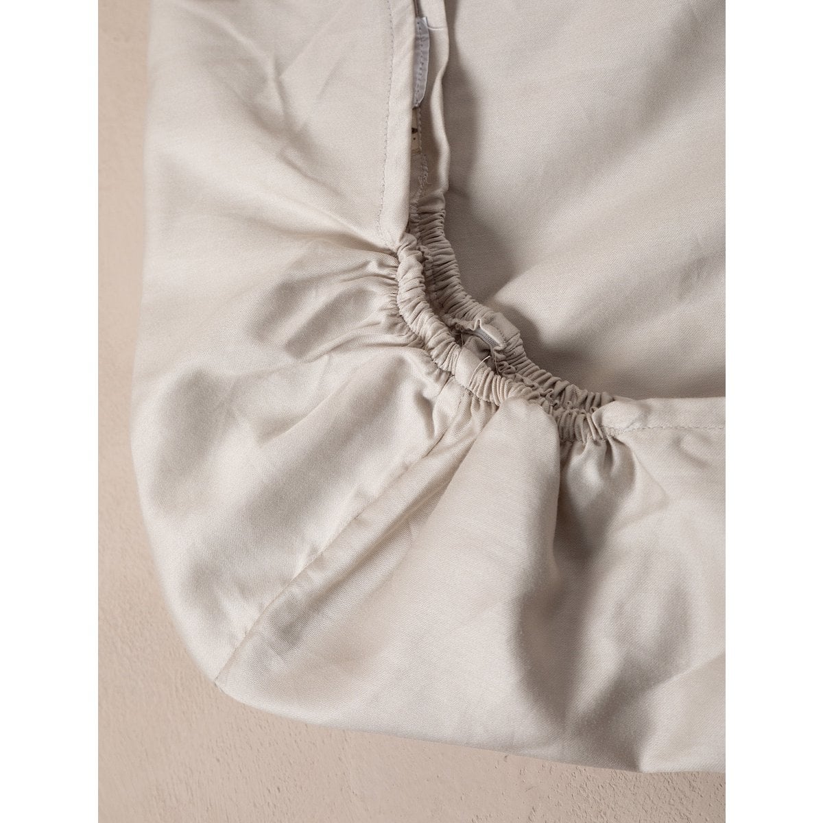 Close-up of a fitted sheet on a bed with a neutral background