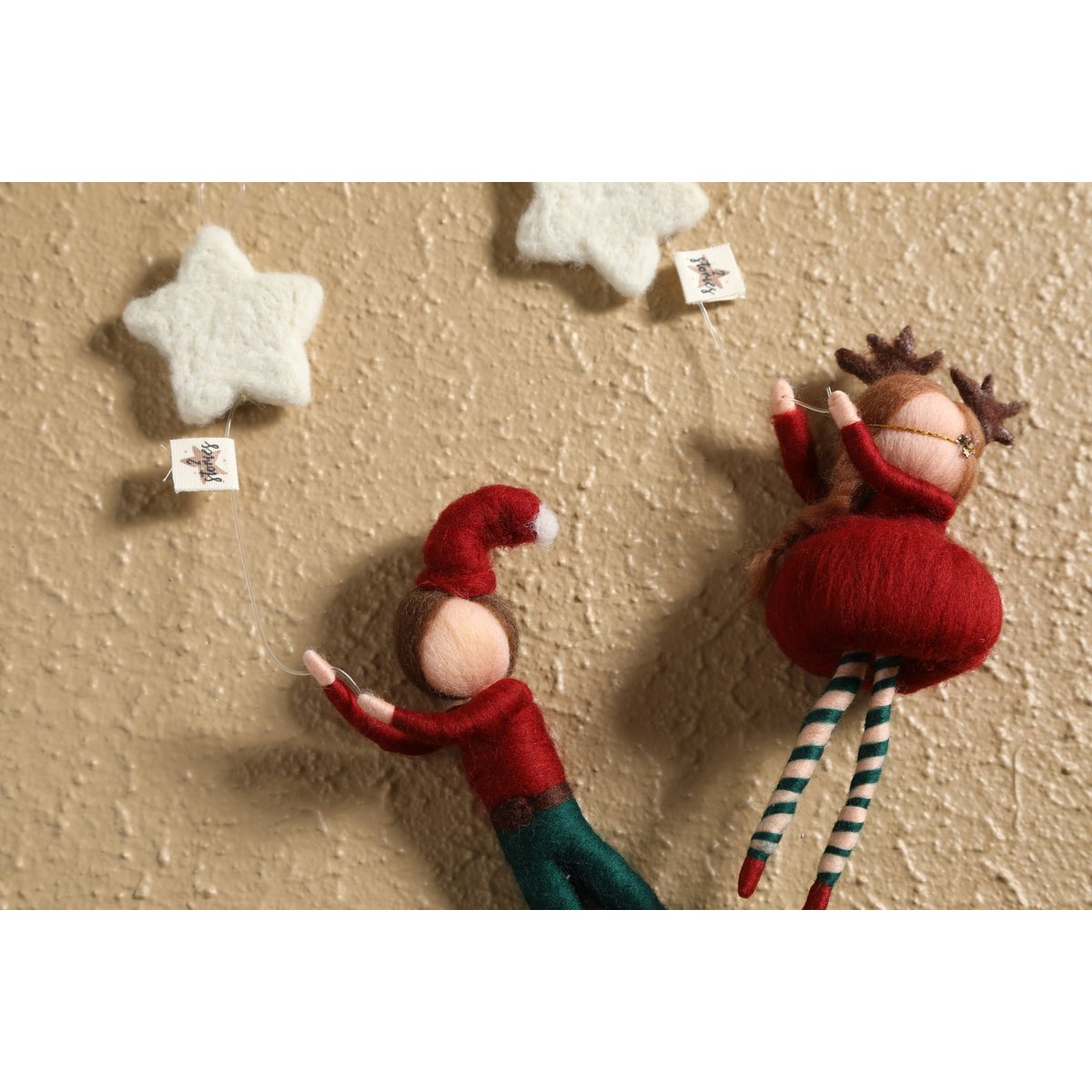 Two small dolls, one resembling an elf and the other a reindeer, on a textured beige surface with star-shaped objects.