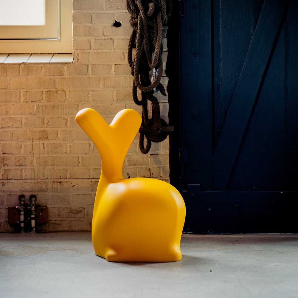 Yellow chair with a unique design in front of a brick wall and dark door.