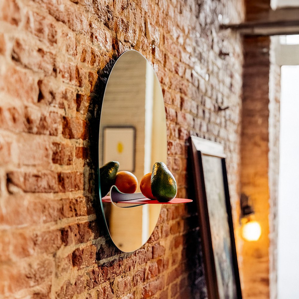 Gold oval mirror on a brick wall with fruits on its surface