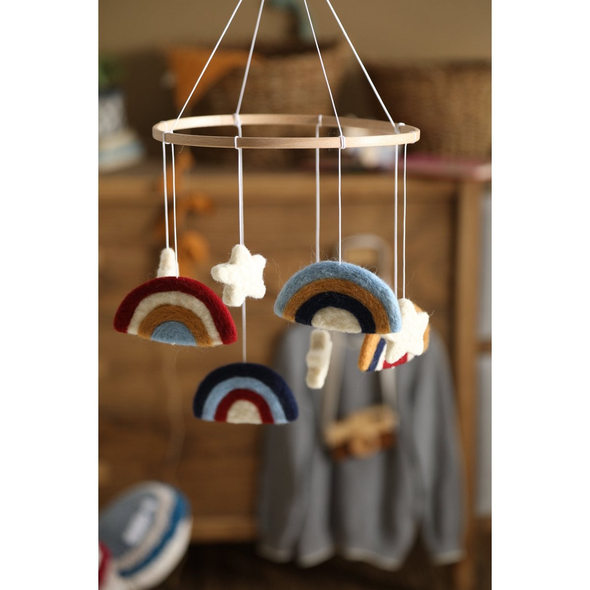 Decorative mobile with rainbow and cloud shapes hanging against a blurred indoor background.