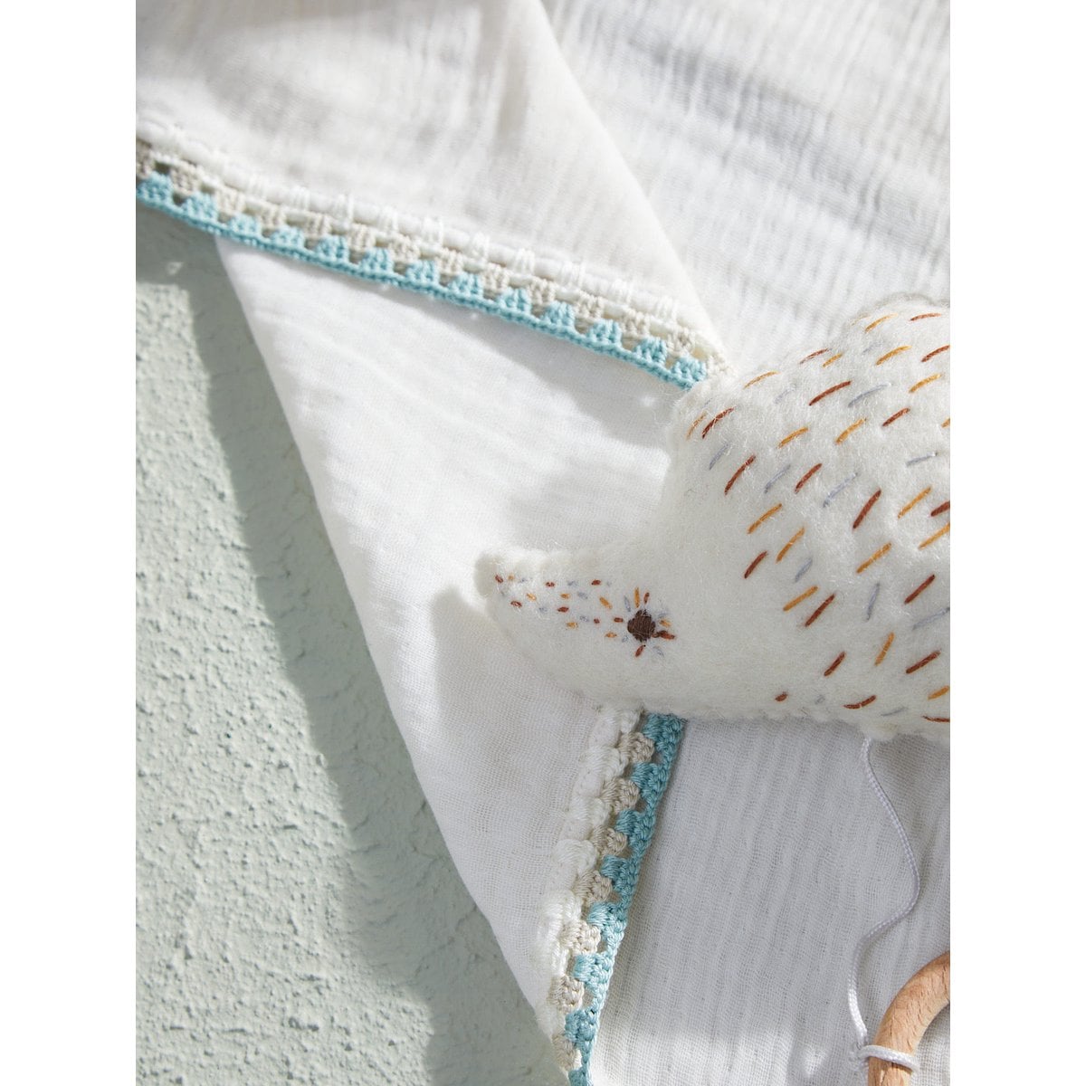 Close-up of a textured white fabric with blue trim and embroidered details on a light background