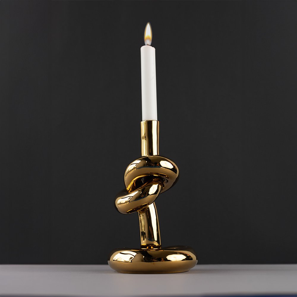 Gold knot candle holder with a lit candle on a dark background