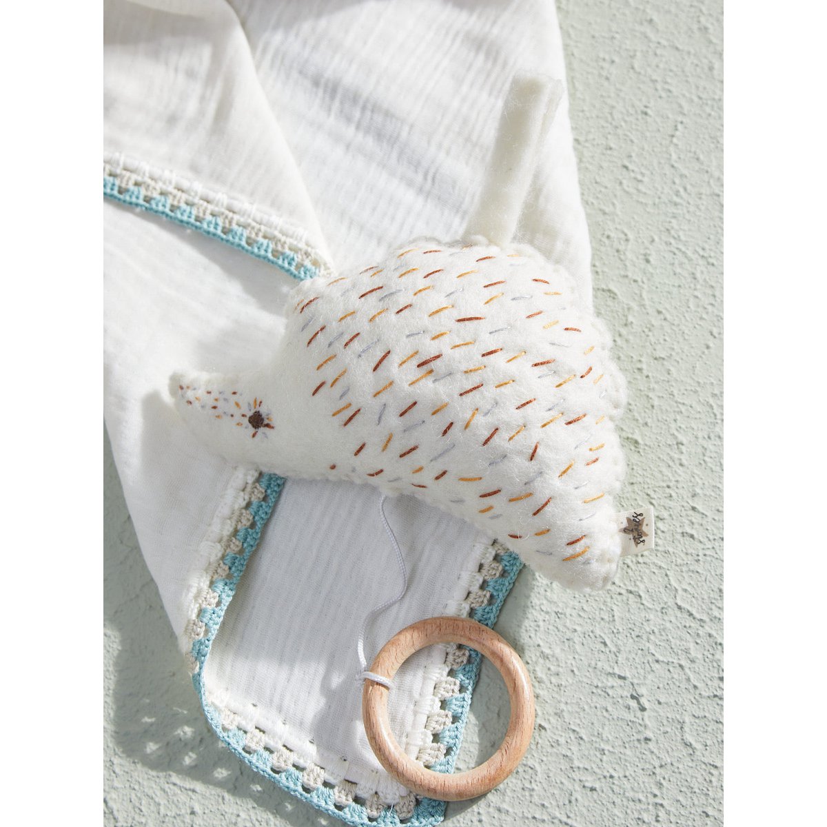 Baby blanket with textured pillow and wooden ring on a light background