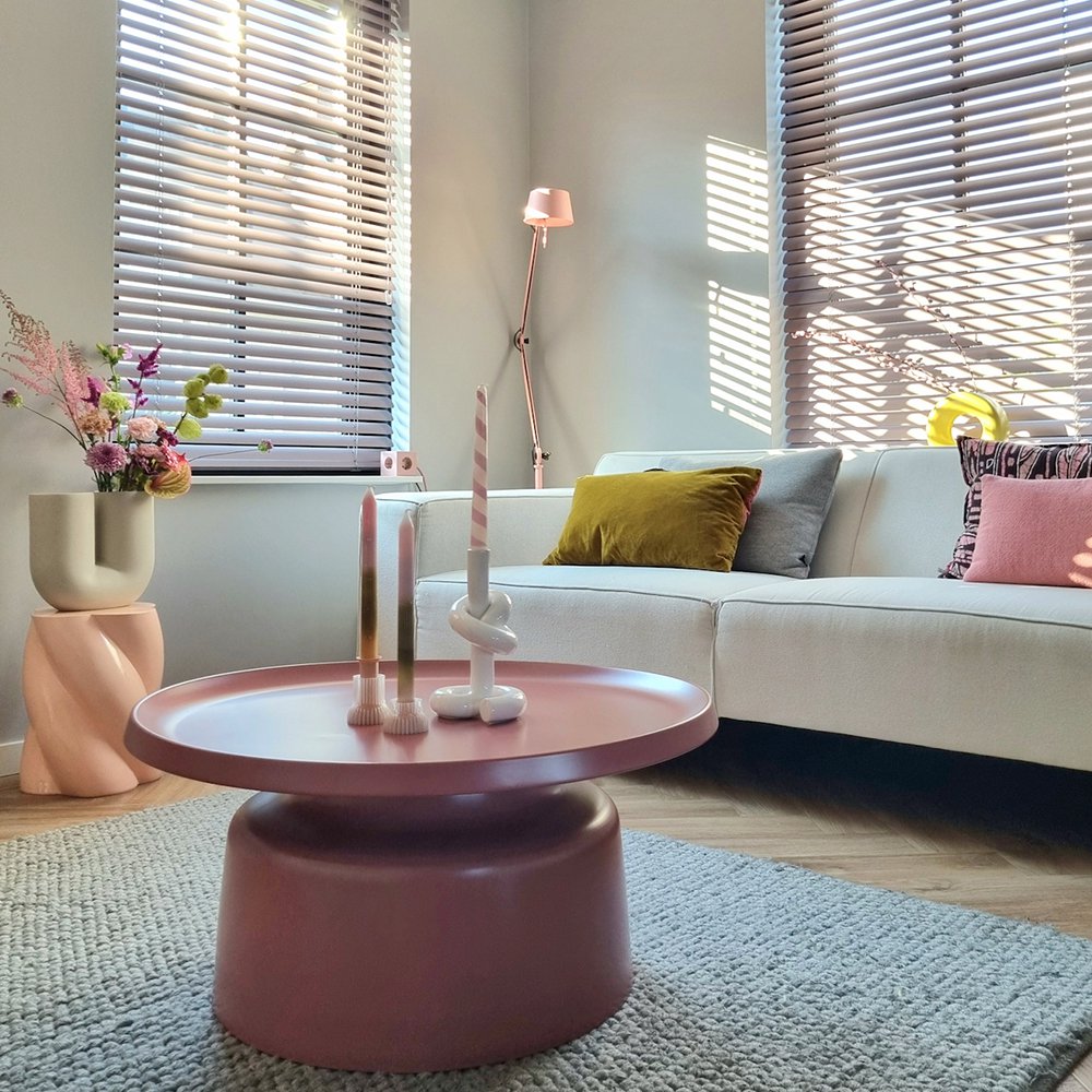 Modern living room with a pink coffee table, white sofa, and decorative pillows and a minimal candle holder.