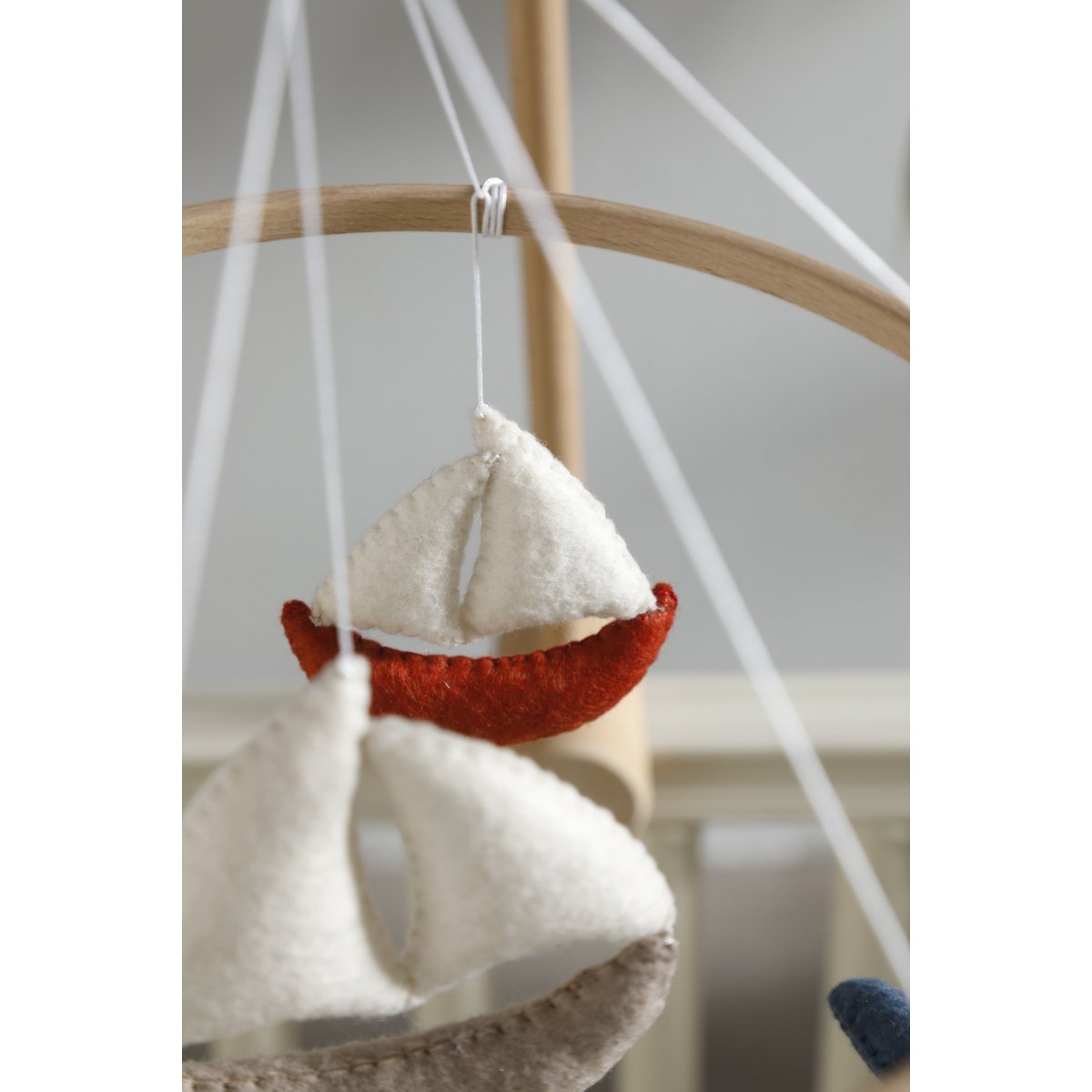 Small sailboat decoration hanging from a string against a neutral background