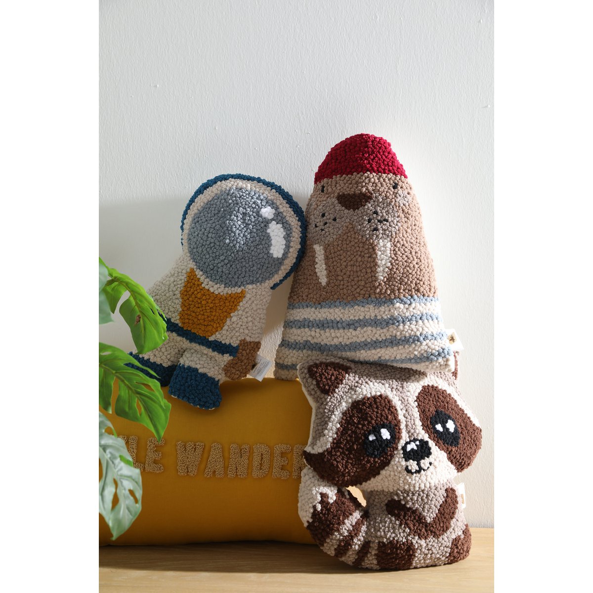 Three knitted or crocheted animal figures on a wooden surface with a plant in the background.