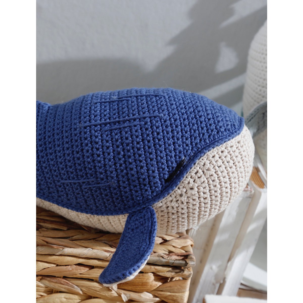 Blue and beige knitted whale toy on a woven surface