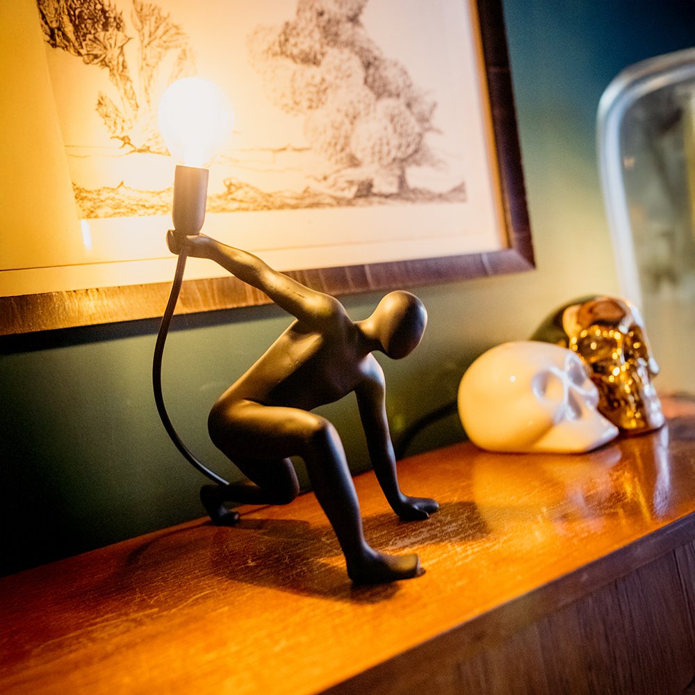 Decorative lamp shaped like a person holding a light bulb on a wooden surface.