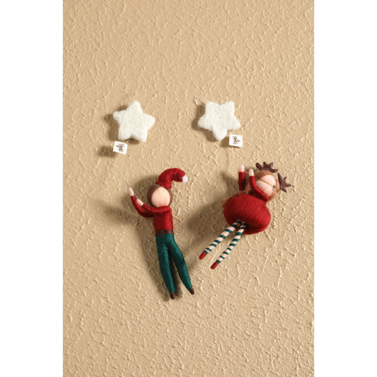 Two decorative elves on a textured beige wall with star-shaped hooks.