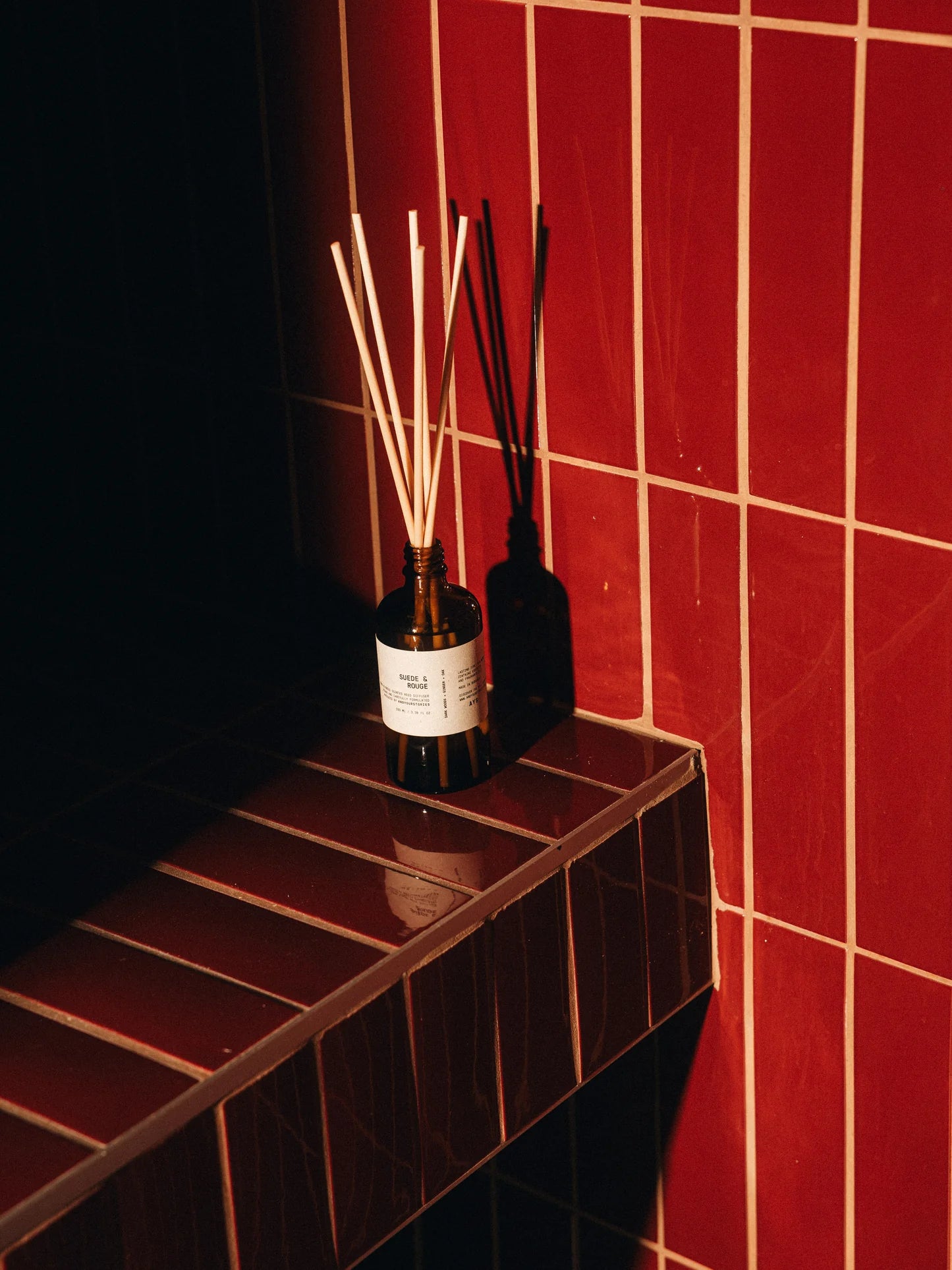 Diffuser with sticks on a dark surface against a red tiled wall
