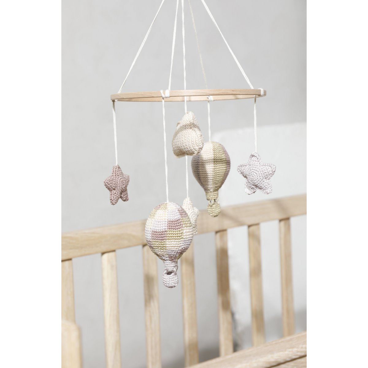 Knitted mobile with stars and hot air balloons hanging above a crib.