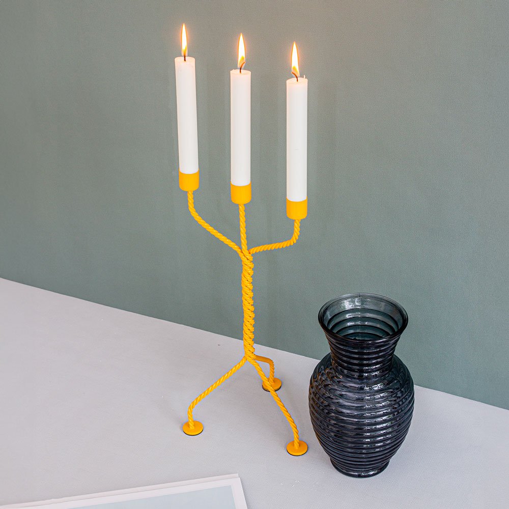 Yellow candle holder with three lit candles on a white surface against a gray wall.