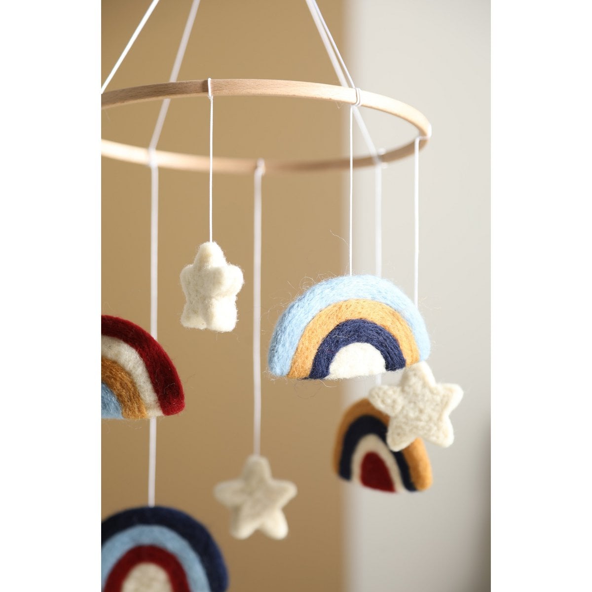 Baby mobile with rainbow and cloud decorations against a beige wall.