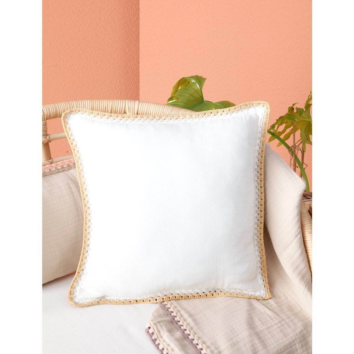 White pillow with decorative trim on a beige couch against a peach wall.