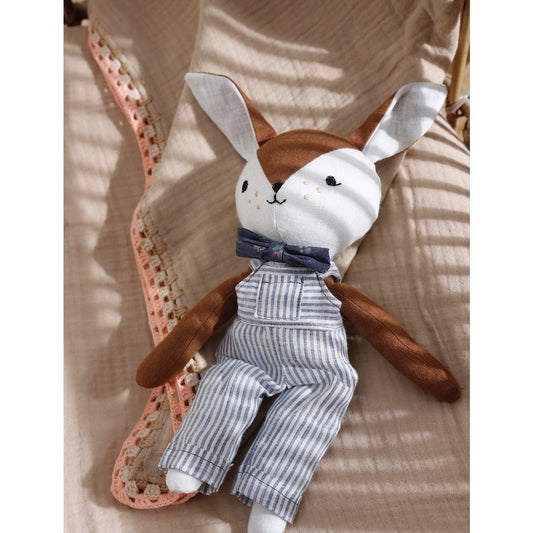 Stuffed toy deer in a striped outfit lying on a textured surface
