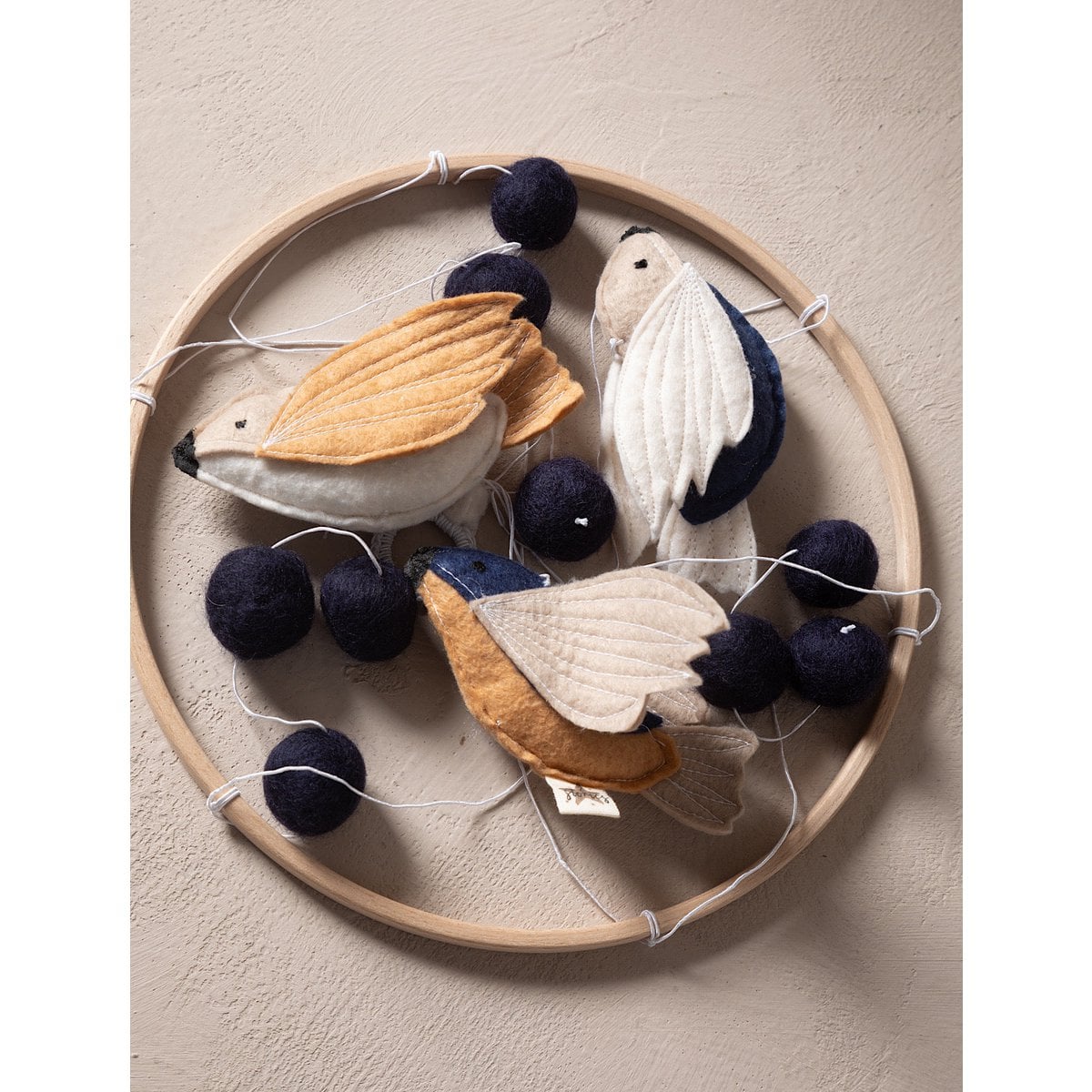Decorative hoop with felt birds and black spheres on a beige background