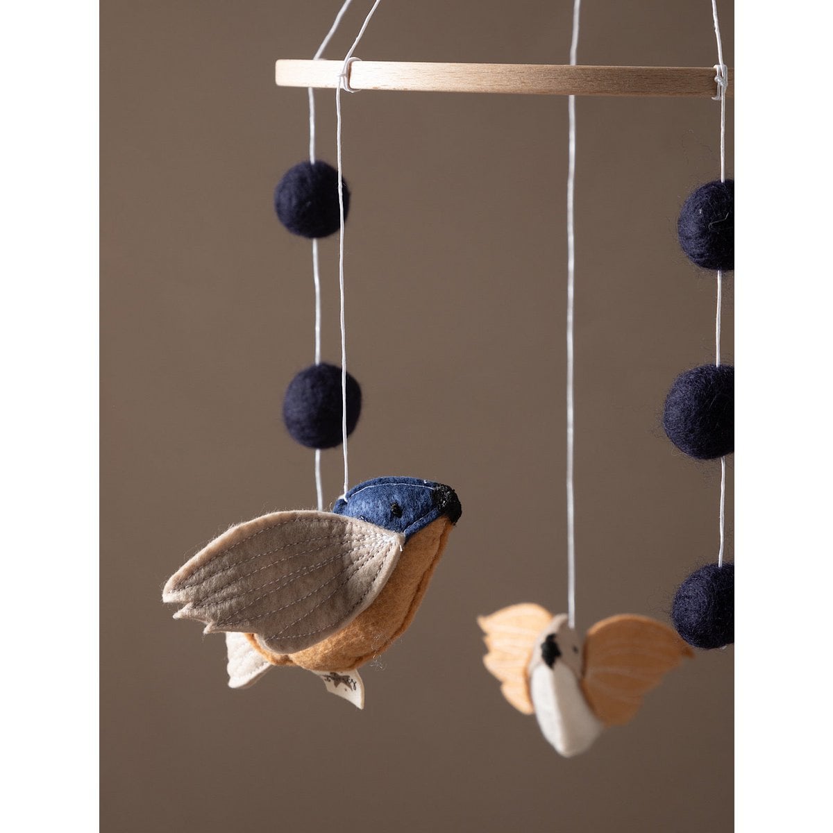 Decorative hanging mobile with birds and pom-poms on a brown background