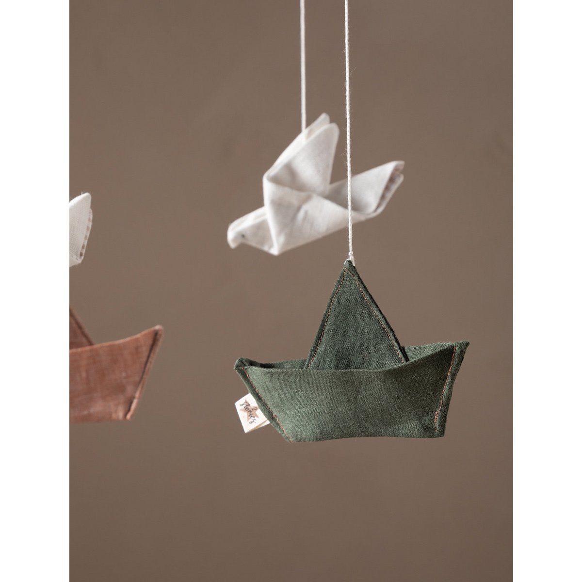Green fabric boat and white bird hanging against a brown background