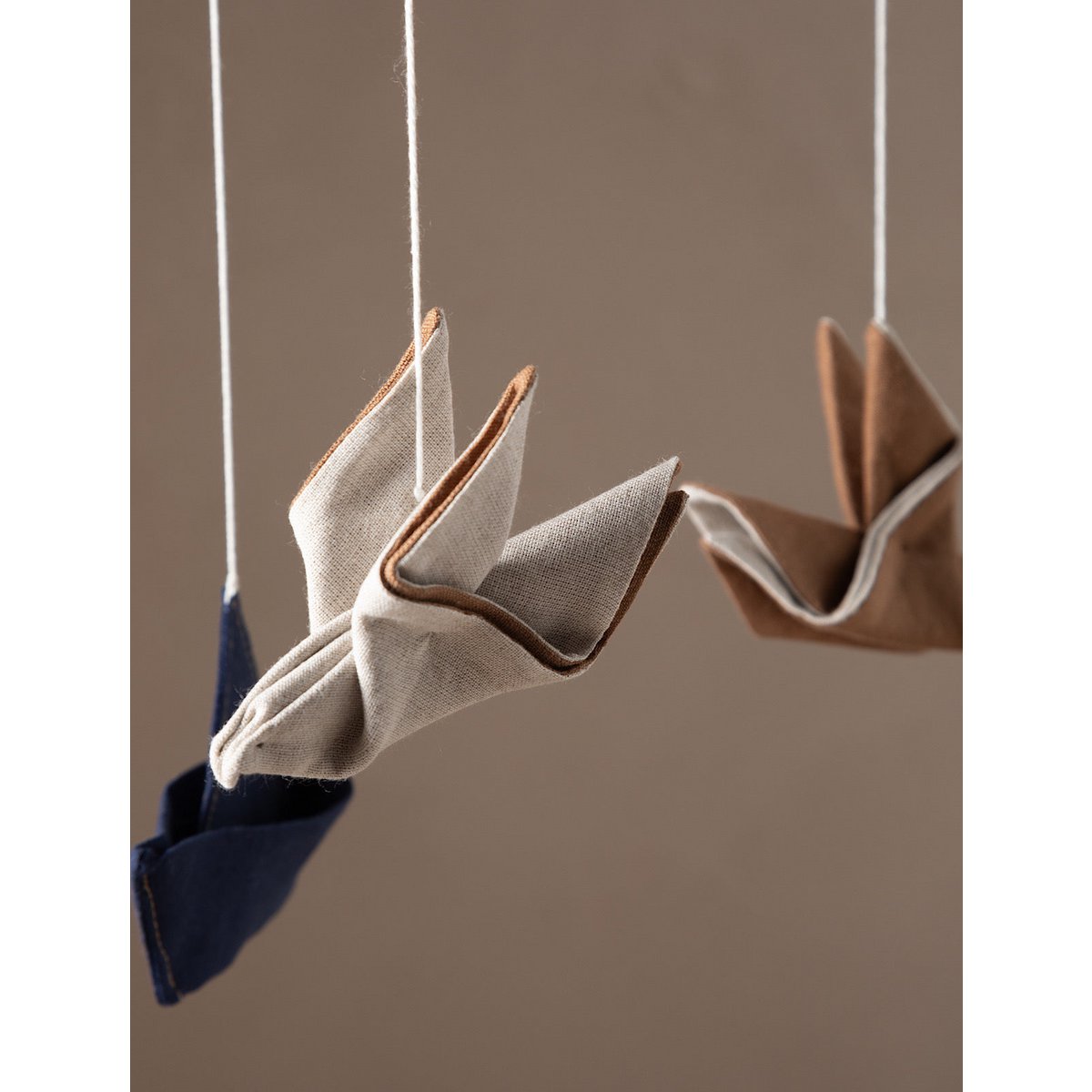 Fabric birds hanging from strings against a neutral background