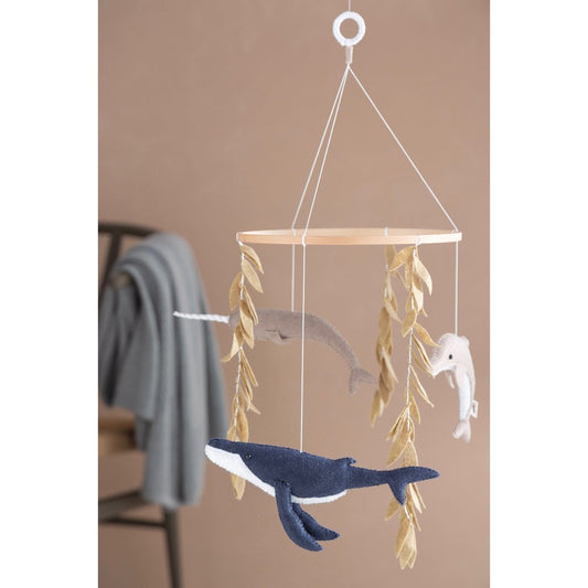 Decorative hanging mobile with whales and leaves on a beige wall.