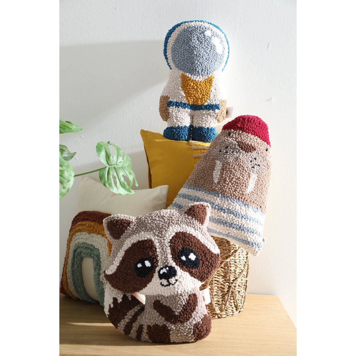 Three knitted animal toys including a raccoon, a bear, and an astronaut on a wooden surface with a plant in the background.
