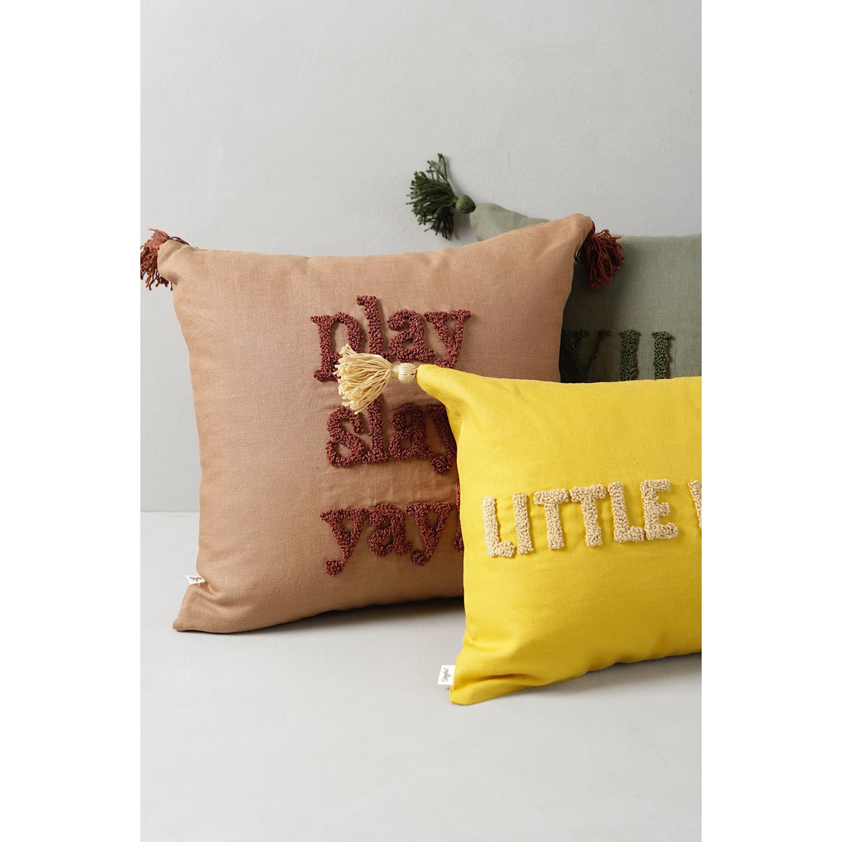 Two decorative pillows, one brown with red text and one yellow with white text, on a light gray surface.