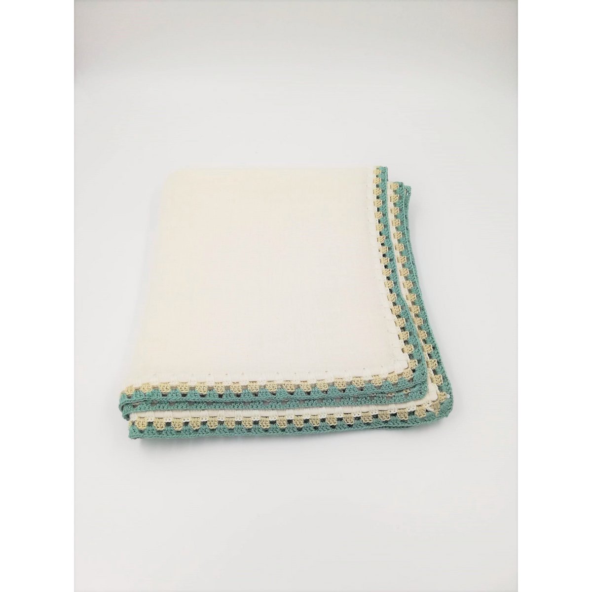 White blanket with green and beige border on a light gray background