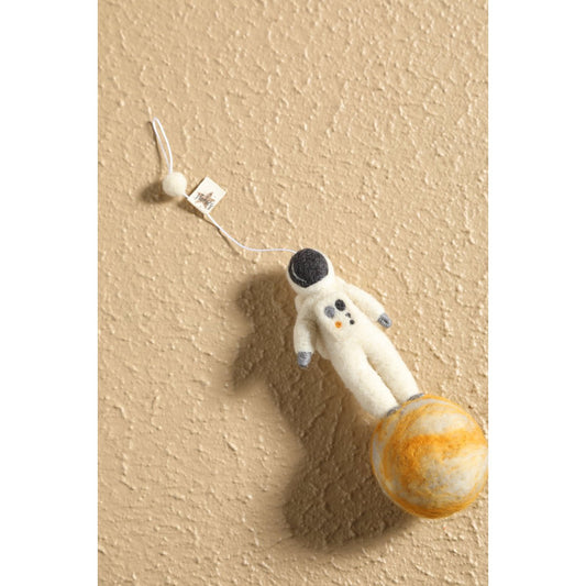 Plush toy astronaut on a planet with a beige wall background