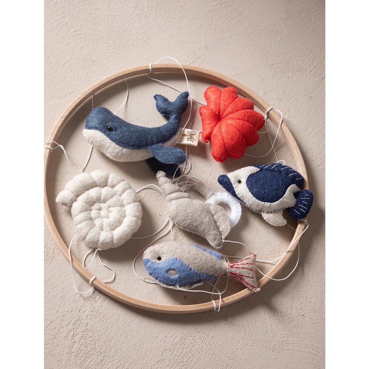Felt sea creature toys hanging on a wooden hoop against a beige background