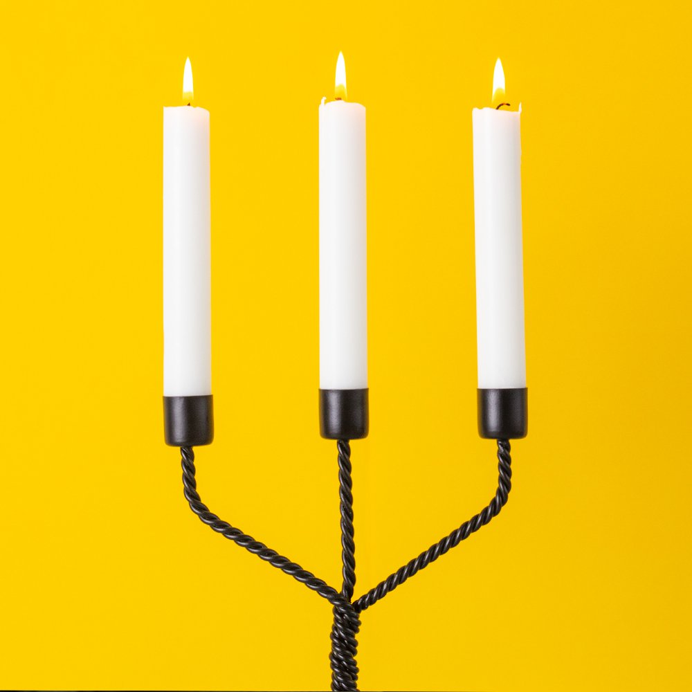 Three white candles in a black candle holder against a yellow background