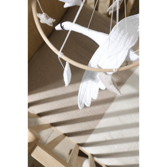 White swan-shaped decorations hanging from a circular wooden frame on a light wooden surface.