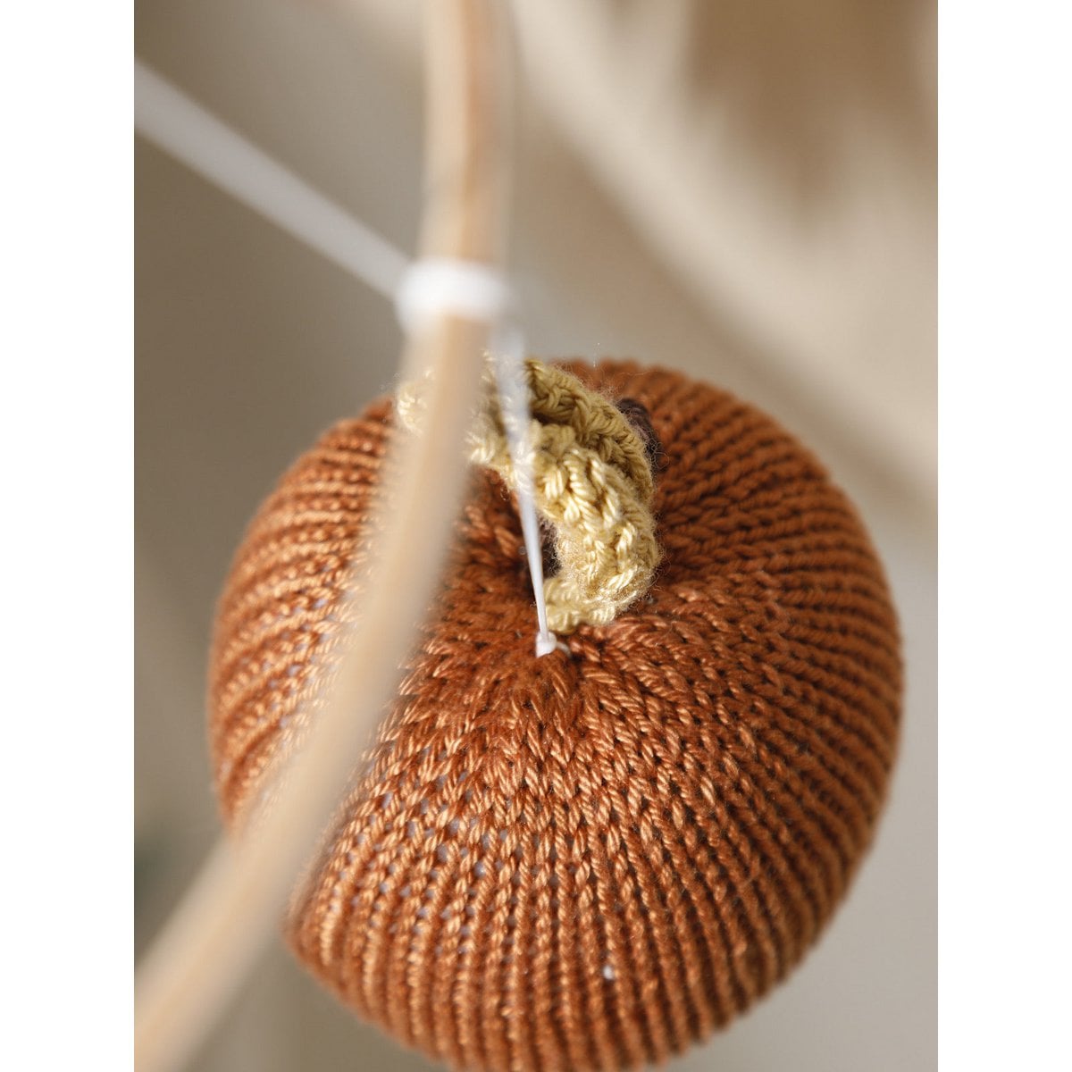 Knitted brown apple-shaped object hanging on a branch with a blurred background
