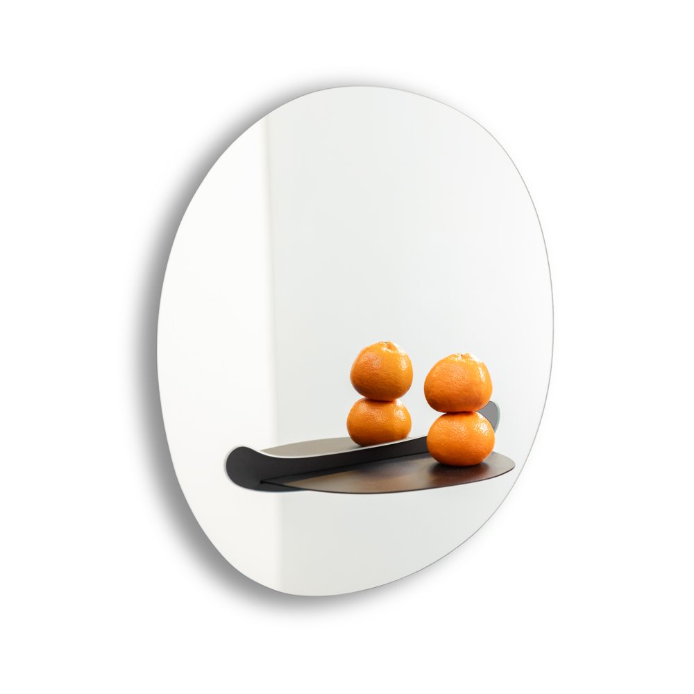 Round mirror with a black shelf holding three oranges on a white background