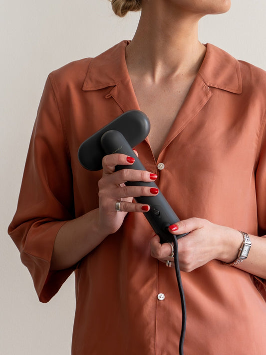 Person holding a handheld steamer against a neutral background