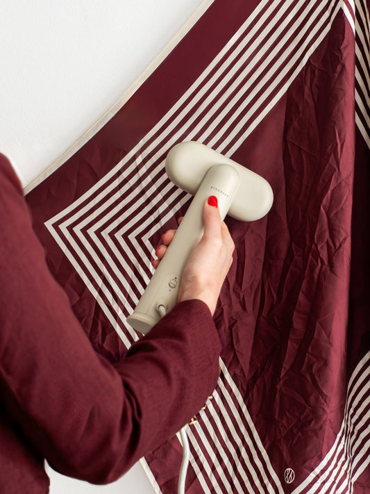 Person using a steam iron by steamery on a maroon fabric with white stripes