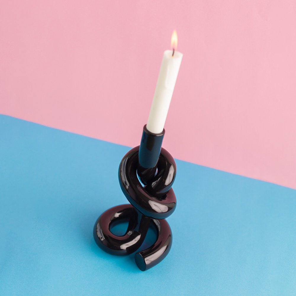 Black spiral candle holder with a white candle on a pink and blue background