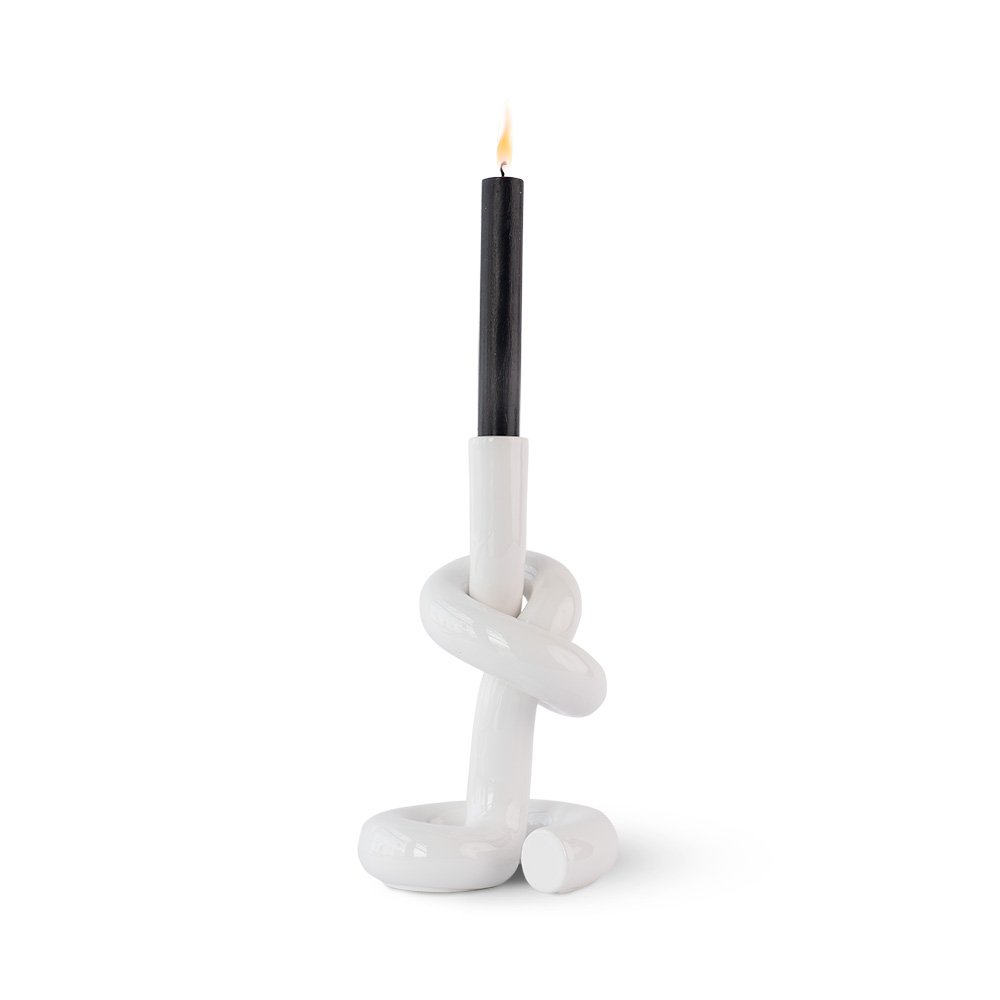 White knot-shaped candle holder with a lit black candle on a white background