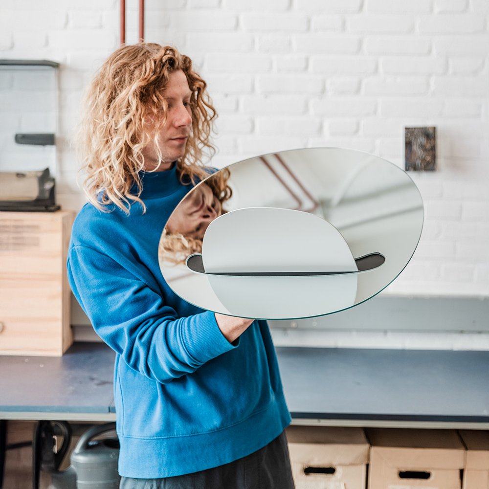 Job van den Bergholding a round mirror with a reflective surface, standing in a kitchen.