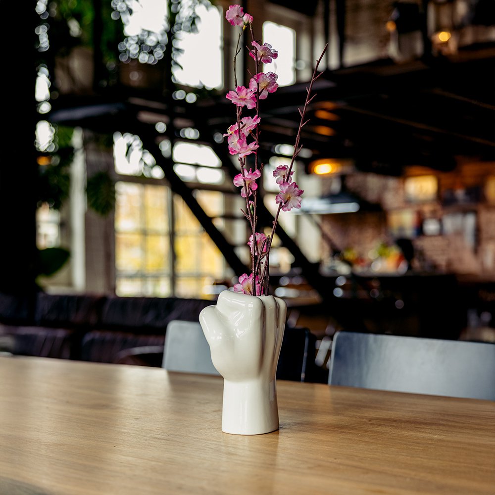 White vase with pink flowers on a wooden table in a restaurant setting