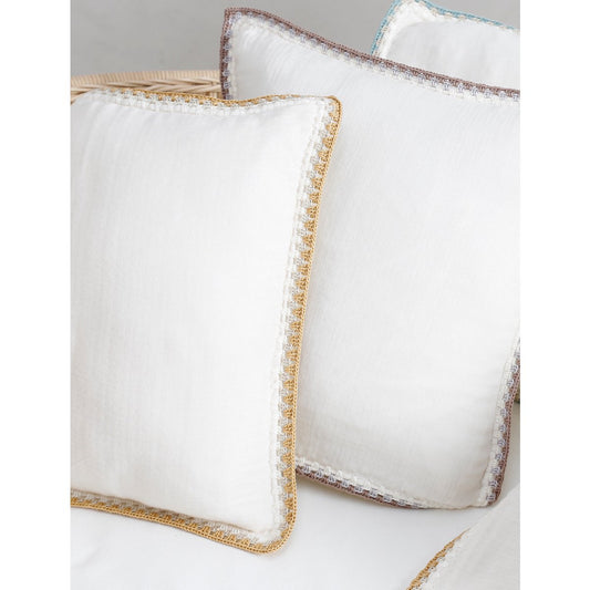 White pillows with gold trim on a light gray background