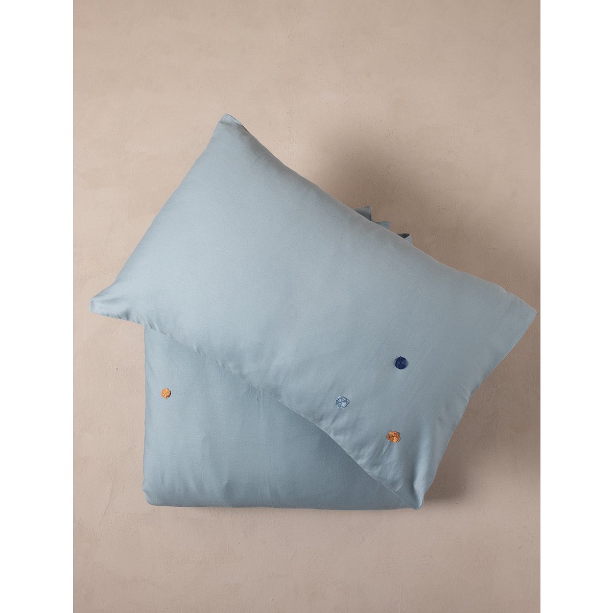 Light blue pillow with decorative buttons on a beige background