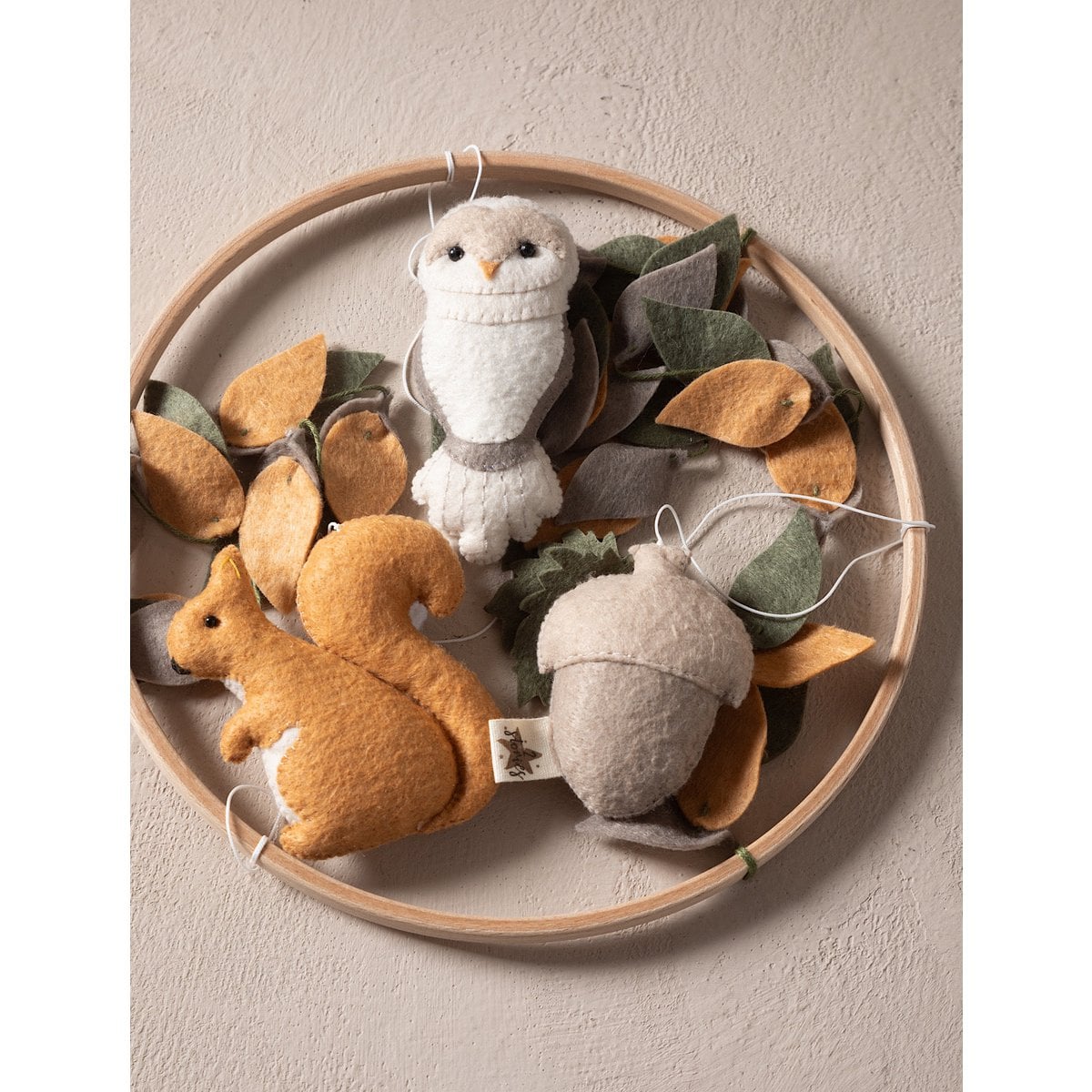 Decorative wreath with felt animals and leaves on a neutral background